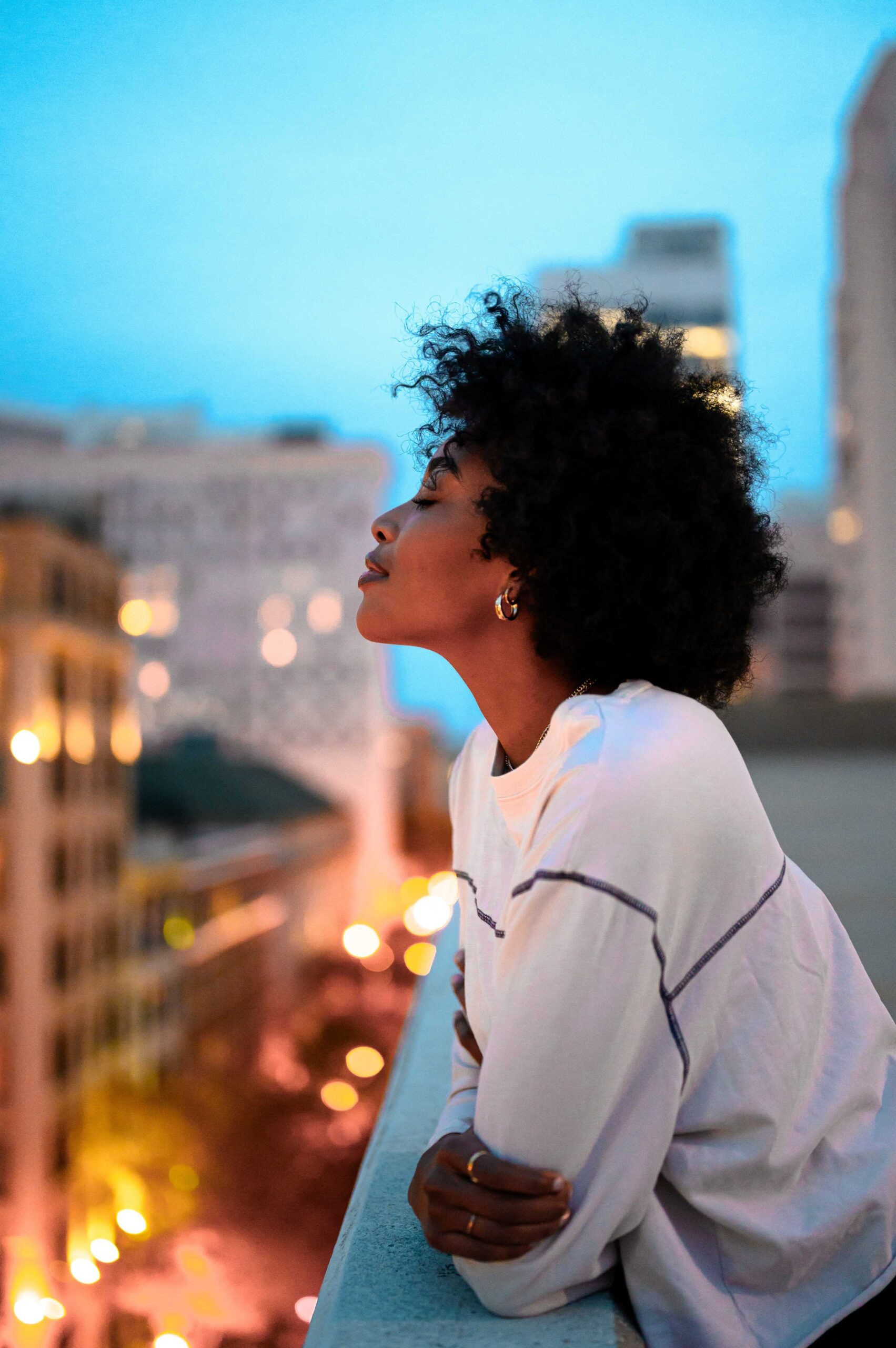 A woman with an afro sitting on a ledge, gazing at the cityscape below her.